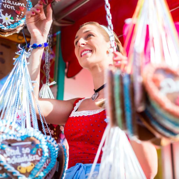 Eine Frau im Dirndl betrachtet Lebkuchenherzen auf einem Markt.