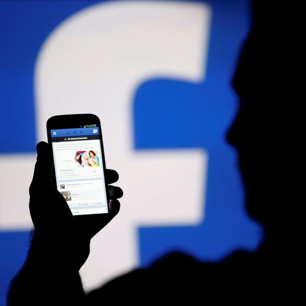 FILE PHOTO: A man is silhouetted against a video screen with a Facebook logo as he poses with a smartphone in this photo illustration