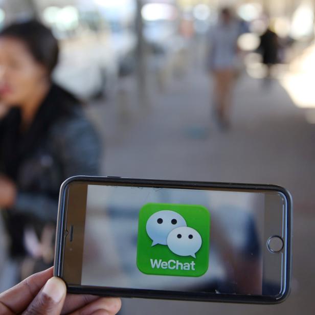 FILE PHOTO - A WeChat logo is displayed on a mobile phone as a woman walks past as she talks on her mobile phone at a taxi rank in this picture illustration