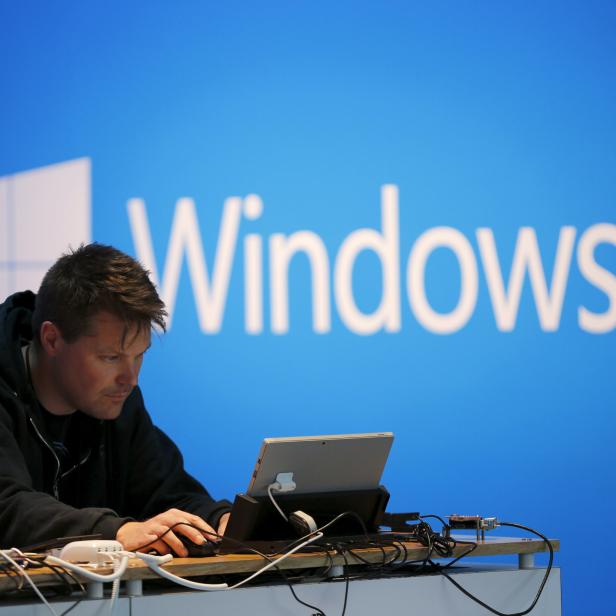 A man works on a laptop computer near a Windows 10 display at Microsoft Build in San Francisco