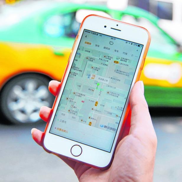 Eine Person hält ein Smartphone mit einer Karten-App in der Hand, im Hintergrund ein Taxi.