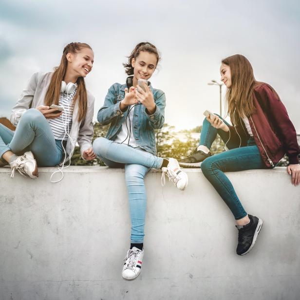 three teenage girls with smartphones on concrete wall