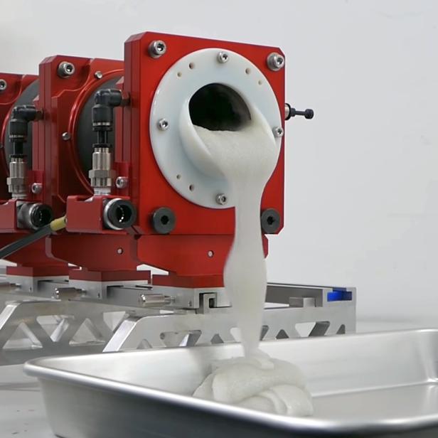 Eine Maschine gießt eine weiße, schaumartige Substanz in eine Metallwanne.