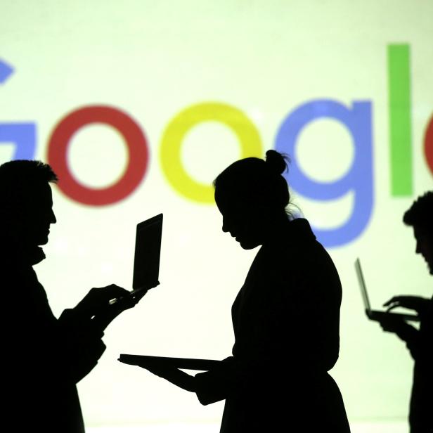 Silhouettes of laptop and mobile device users are seen next to a screen projection of Google logo in this picture illustration