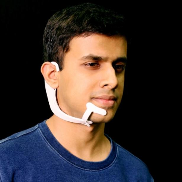 Ein Mann trägt ein weißes, futuristisch anmutendes Gerät um seinen Hals und sein Ohr.