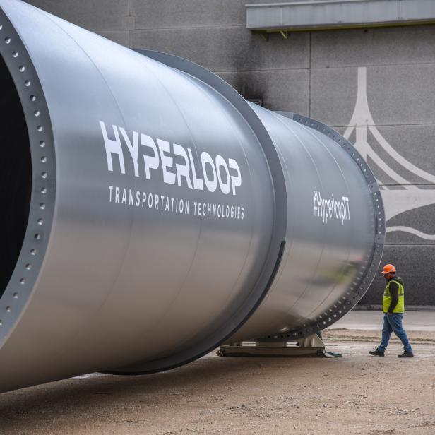 Ein Arbeiter geht an einem großen Rohr mit der Aufschrift „Hyperloop Transportation Technologies“ vorbei.