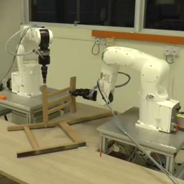 Zwei Roboterarme montieren ein Holzgestell in einer Werkstatt.