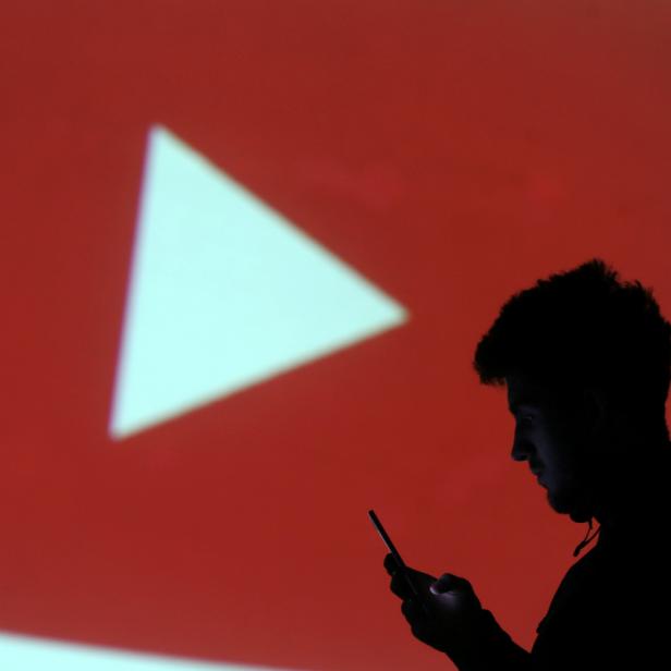 Silhouette of mobile user is seen next to a screen projection of Youtube logo in this picture illustration