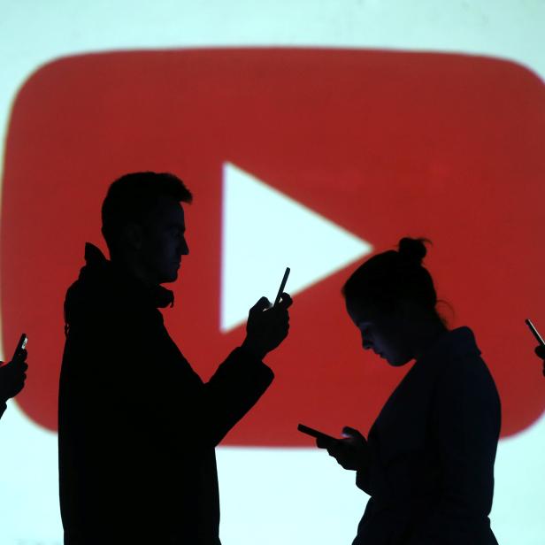 Silhouettes of mobile users are seen next to a screen projection of Youtube logo in this picture illustration