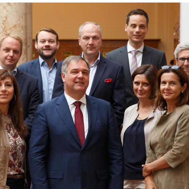 Eine Gruppe von neun Personen posiert für ein Gruppenfoto in einem Gebäude.