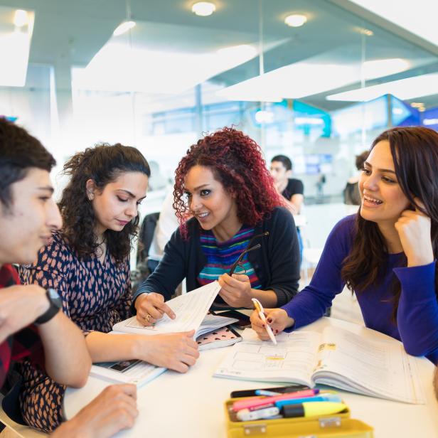 Eine Gruppe Studenten sitzt an einem Tisch und arbeitet zusammen an ihren Büchern.