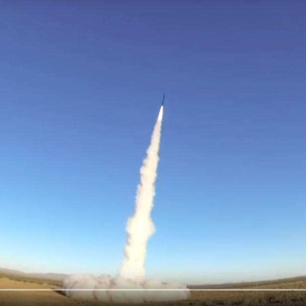 Eine Rakete startet mit einer Rauchwolke in den blauen Himmel.