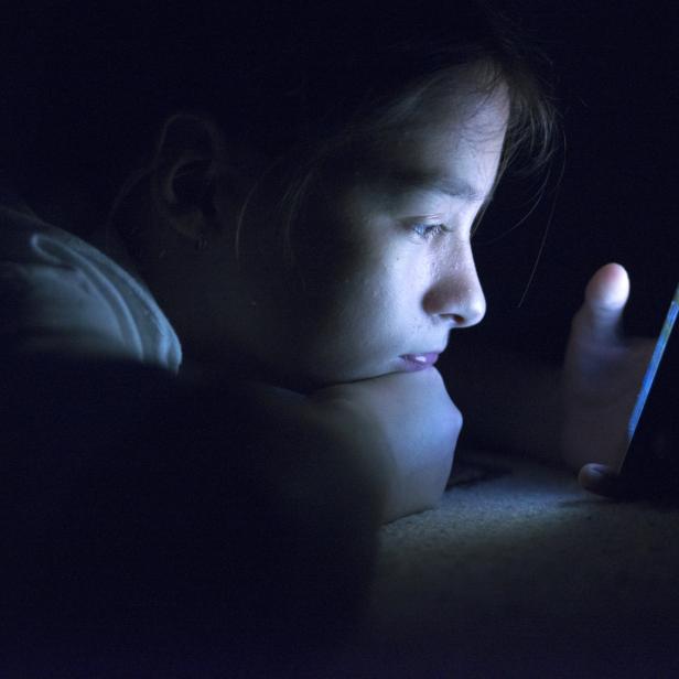 Teenager sending email from smart phone in her bed