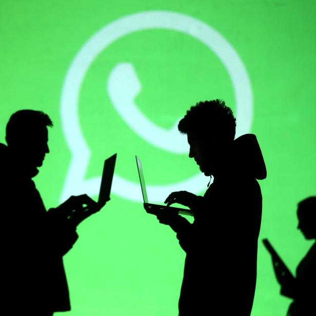 Silhouettes of laptop and mobile device users are seen next to a screen projection of Whatsapp logo in this picture illustration