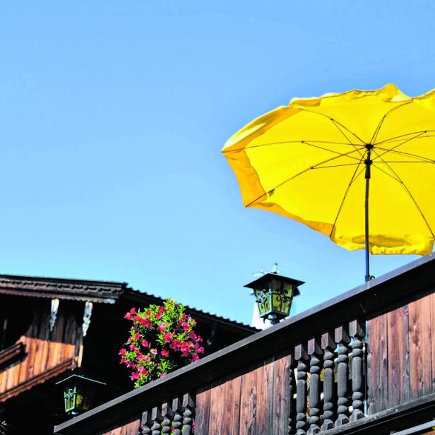 Ein gelber Sonnenschirm auf dem Balkon eines Holzhauses vor blauem Himmel.