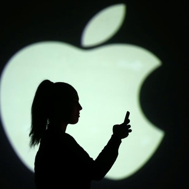 Silhouette of mobile user is seen next to a screen projection of Apple logo in this picture illustration