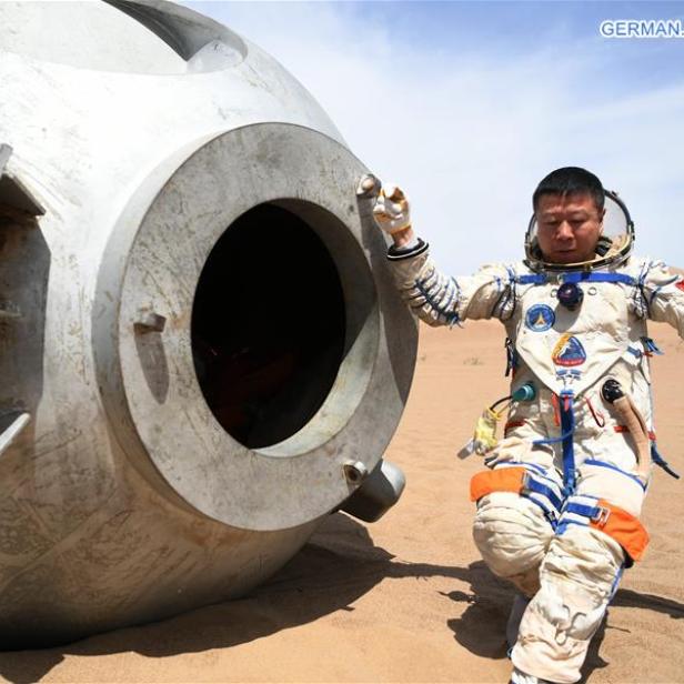 Ein Astronaut steht neben einer gelandeten Raumkapsel in einer Wüste.