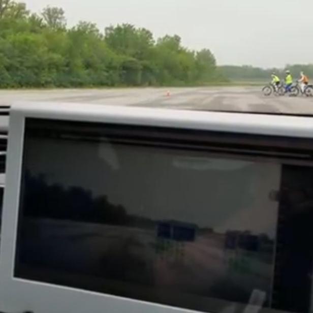 Aus dem Inneren eines Autos werden Radfahrer auf einer Landstraße beobachtet.