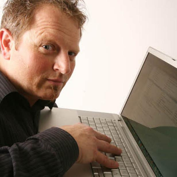 Ein Mann blickt über die Schulter, während er an einem Laptop tippt.