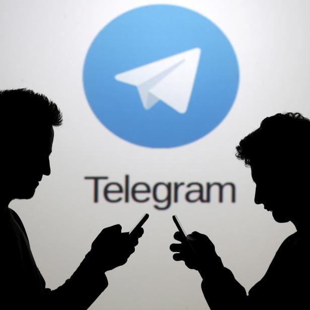 FILE PHOTO: Men pose with smartphones in front of a screen showing the Telegram logo in this picture illustration