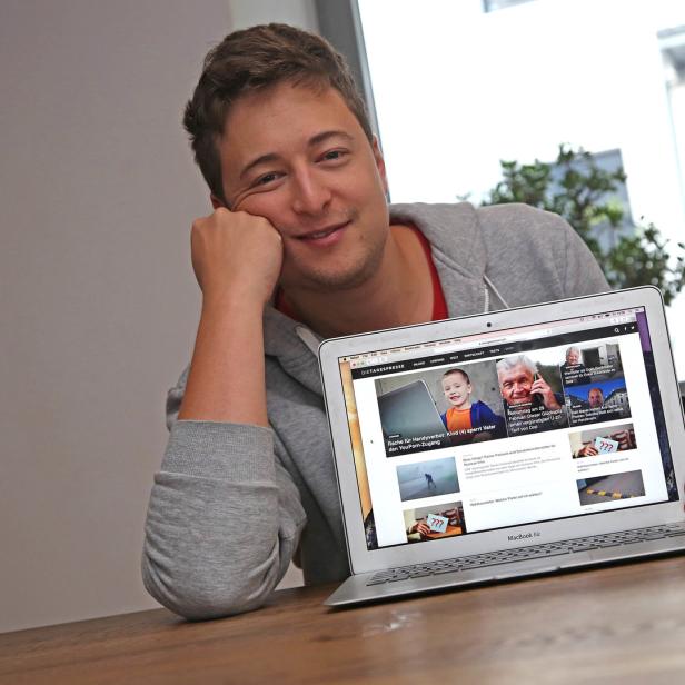 Ein Mann lehnt an einem Tisch und hält einen Laptop mit der Webseite „Die Tagespresse“ in der Hand.