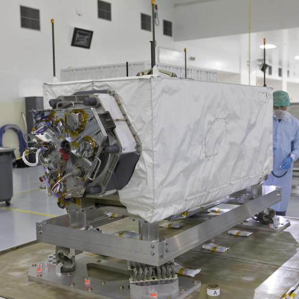 Ein Satellitenteil, teilweise mit einer weißen Schutzhülle bedeckt, steht in einem Reinraum.