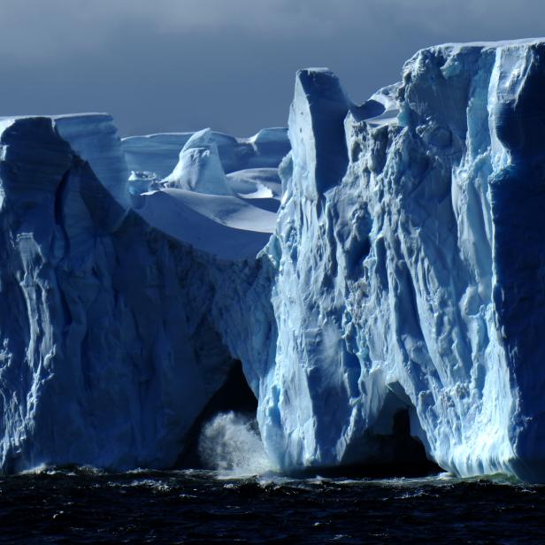 Ein massiver Eisberg mit einer Höhle, in der das Wasser spritzt.