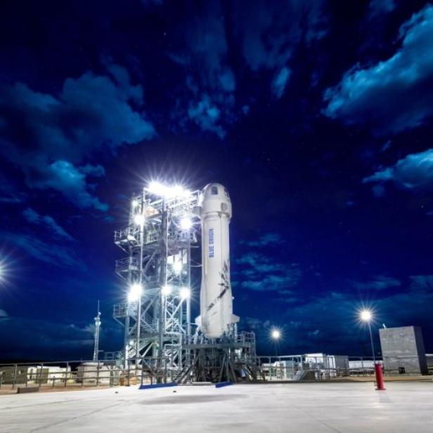 Eine Blue Origin Rakete steht nachts auf einer Startrampe unter einem bewölkten Himmel.