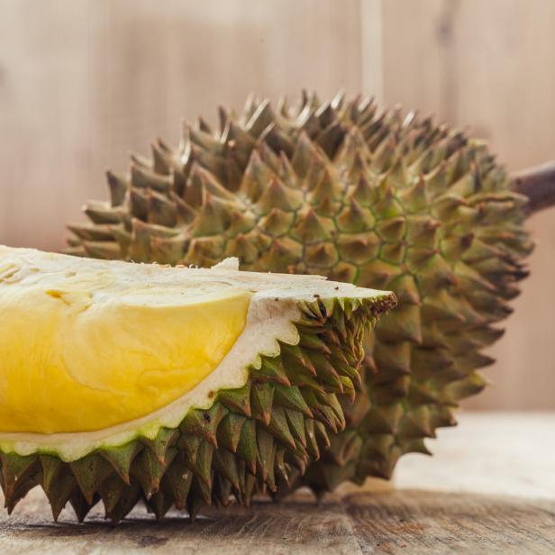 Eine Durian-Frucht, angeschnitten, liegt auf einem Holztisch.