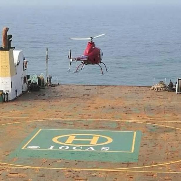 Ein roter Hubschrauber landet auf dem Deck eines Schiffes mit der Aufschrift IOCAS.
