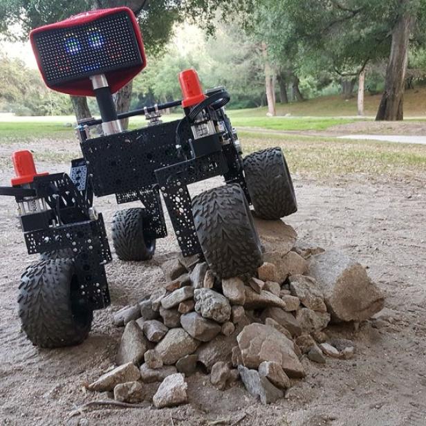 Ein vierrädriger Roboter fährt über einen Steinhaufen in einem Park.
