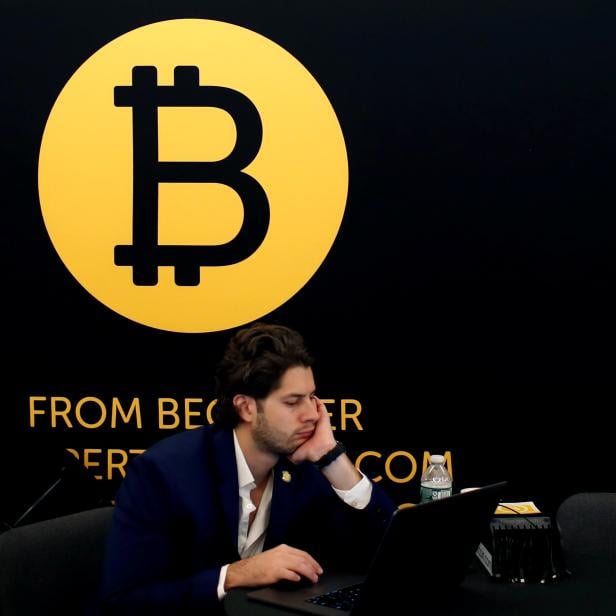 A man works on a laptop beneath the Bitcoin logo at the Consensus 2018 blockchain technology conference in New York City