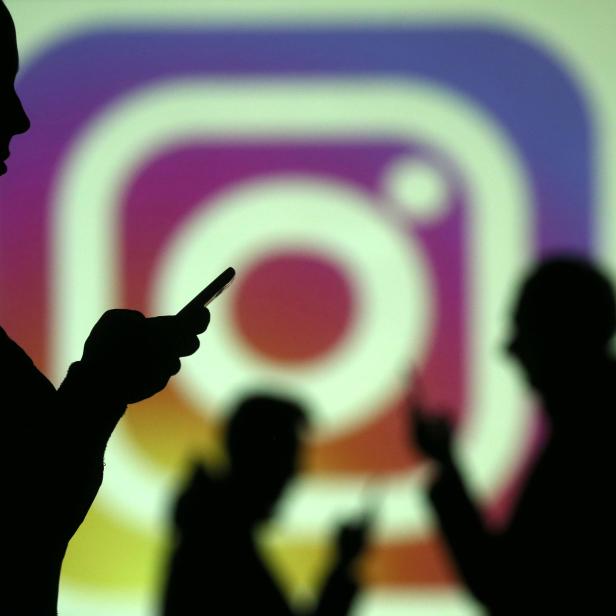 Silhouettes of mobile users are seen next to a screen projection of Instagram logo in this picture illustration