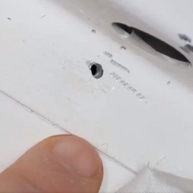 Ein Finger zeigt auf ein kleines Loch in einer weißen Oberfläche.