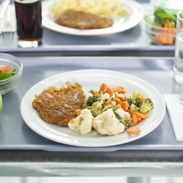 Ein Tablett mit einem Teller mit Gemüse und einem Leibchen sowie einem Apfel und Salat und Wasser.