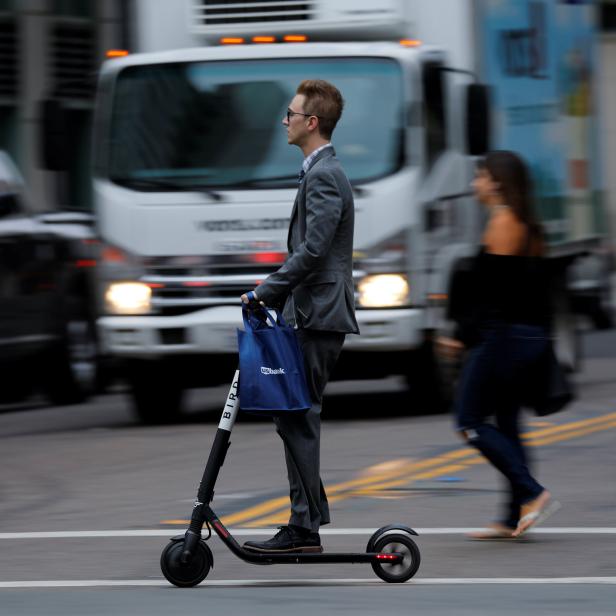 A man in a suit rides an electric BIRD rental scooter along a city street in San Diego, California