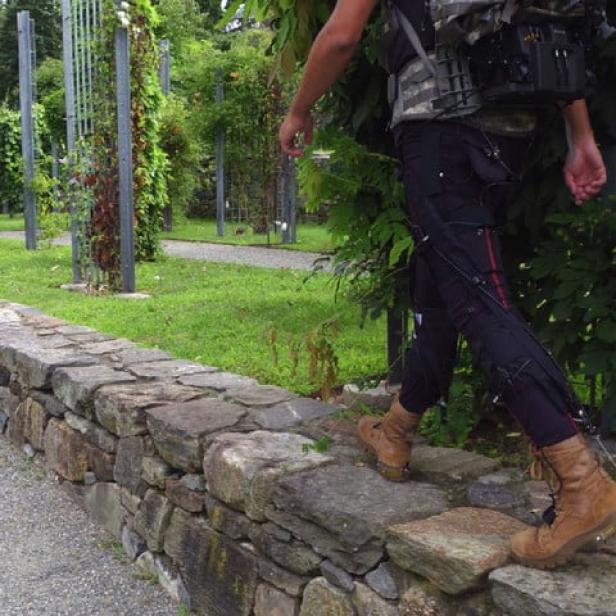 Eine Person mit Stiefeln balanciert auf einer Steinmauer in einem Garten.