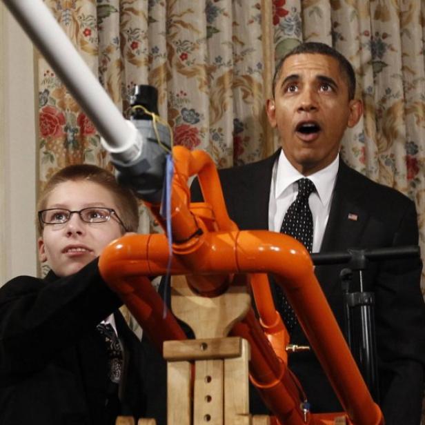 Ein Junge bedient eine Apparatur, während Barack Obama überrascht daneben steht.