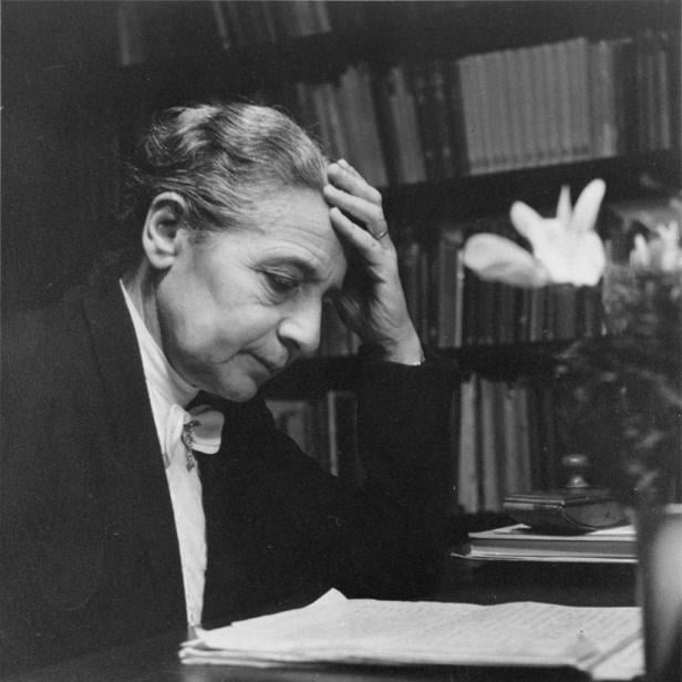 Eine ältere Frau sitzt an einem Schreibtisch und denkt nach.