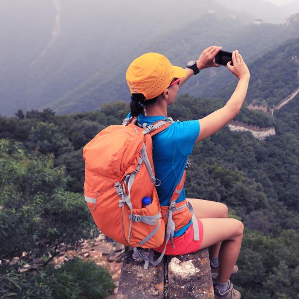 young woman hiker taking photo with smart phone on top of great wall