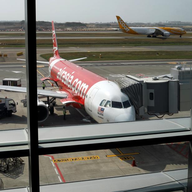 A Scoot airplane takes off past an Airasia airplane at Changi Airport Terminal 4 in Singapore