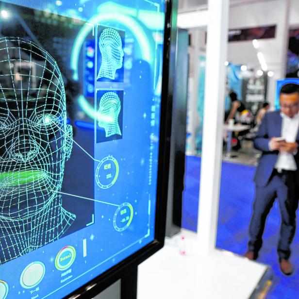 Visitors check their phones behind the screen advertising facial recognition software during Global Mobile Internet Conference (GMIC) at the National Convention in Beijing