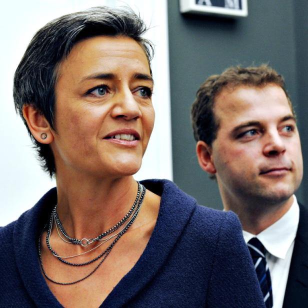 Eine Frau mit kurzem, dunklem Haar und ein Mann im Anzug schauen zur Seite.