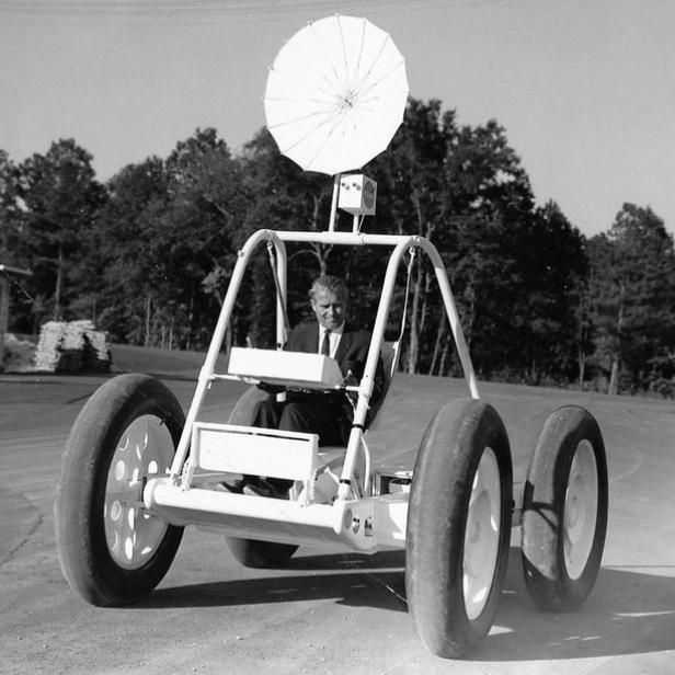 Ein Mann fährt ein ungewöhnliches Fahrzeug mit großen Reifen und einer Antenne auf einer Straße.