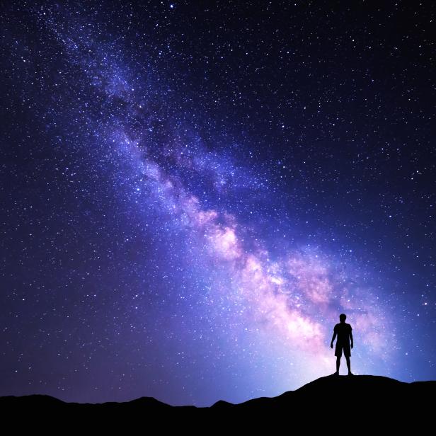 Nachthimmel mit Milchstraße und der Silhouette eines stehenden Mannes.