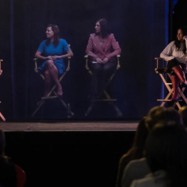 Fünf Frauen sitzen auf Regiestühlen auf einer Bühne vor Publikum.