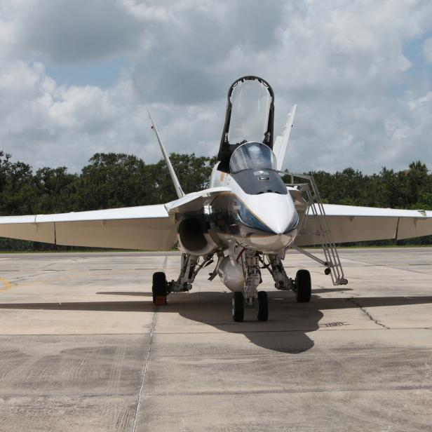 Ein weißes Kampfflugzeug steht mit geöffnetem Cockpit auf einem Flugfeld.