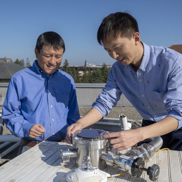 Zwei Männer arbeiten auf einem Dach an einer wissenschaftlichen Apparatur.