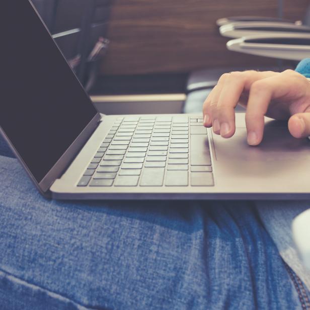 Hand of a young man in jeans working on a laptop in transport close-up. Photo toned in the style of instagram.