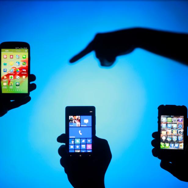 FILE PHOTO: Men are silhouetted against a video screen as they pose with smartphones